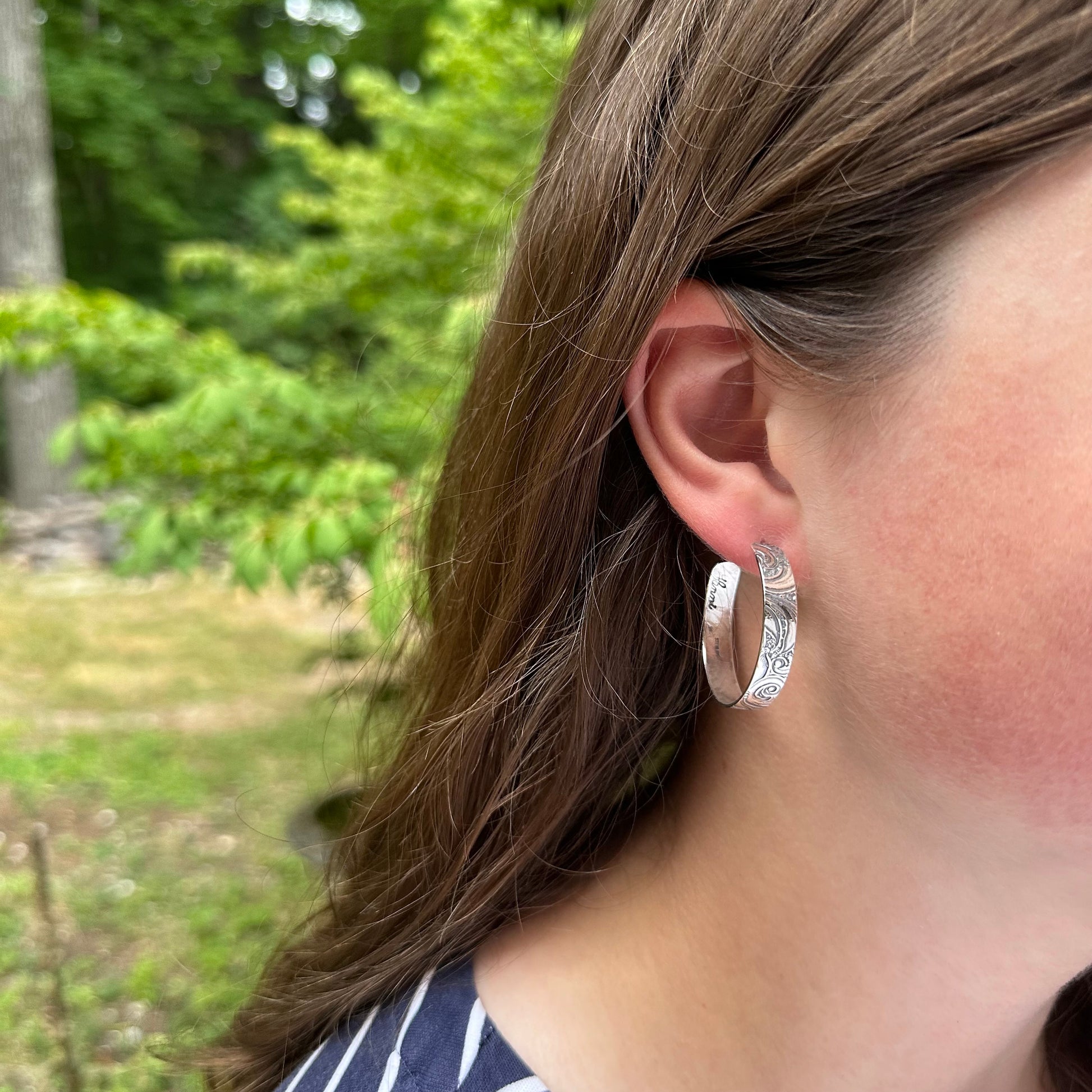 On model : sterling silver post hoop earring with engraved scroll pattern impressed from a vintage scroll and swirl pattern. 1/4 inch wide by your choice of diameter, handmade earrings with push back by Hanni jewelry harbor springs, Michigan